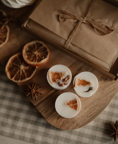 Three winter wax melts topped with dried orange and star anise beside a wrapped kraft box