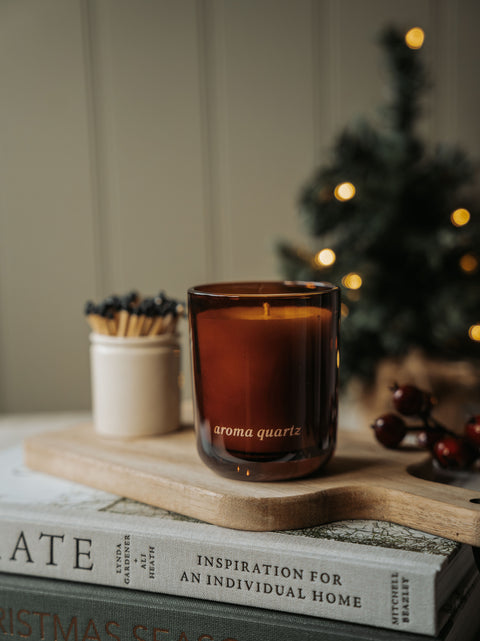 Winter Orchards amber glass candle on a wooden board with a matchstick pot and a Christmas tree behind