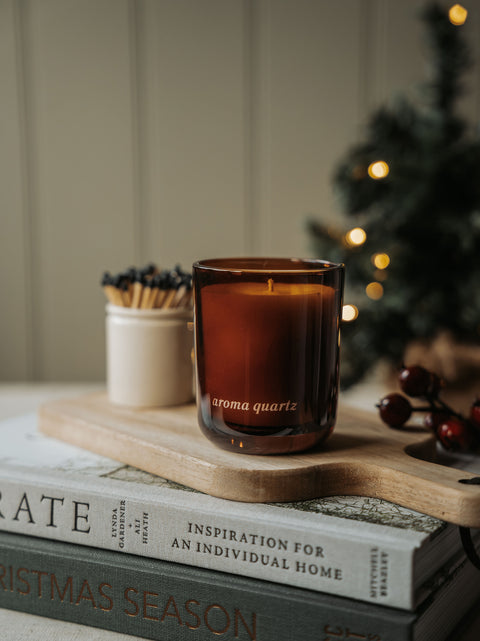 Winter Orchards candle styled on a stack of books with red berries and warm fairy lights