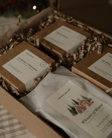 Open gift box with three small boxes and a Whisper of Winter wax melt packet in shredded paper