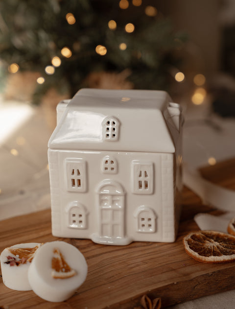Ceramic house wax melt warmer with the roof on, styled with winter wax melts and dried orange