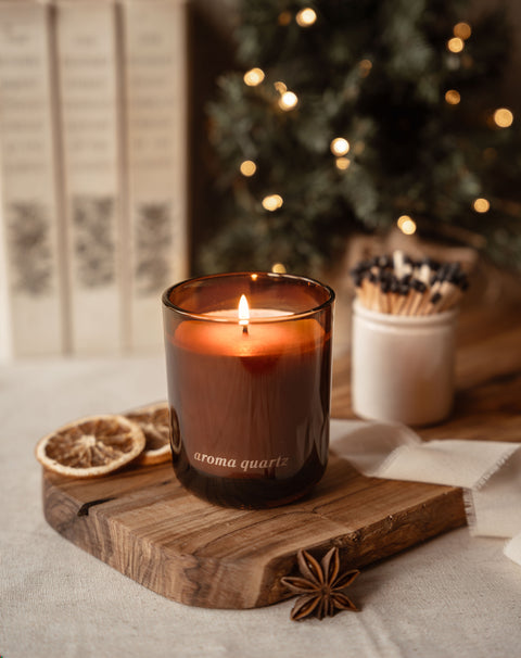 Aroma Quartz winter candle lit on an olive wood board with star anise, dried orange and a matchstick pot