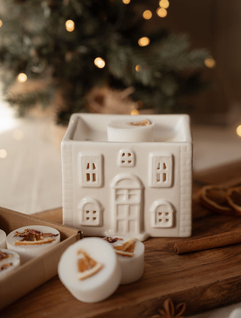 Cream ceramic house wax melt warmer with a winter wax melt in the dish and a tealight below