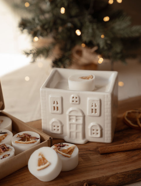 Ceramic house wax melt warmer in front of a Christmas tree with fairy lights