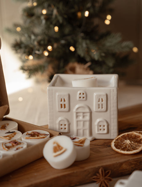 Ceramic house wax melt warmer beside a box of winter wax melts and cinnamon sticks