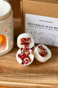 a stack of natural wax melts with botanical elements on a wooden surface next to an oil