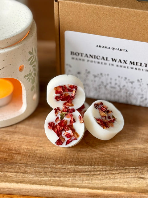a stack of natural wax melts with botanical elements on a wooden surface next to an oil