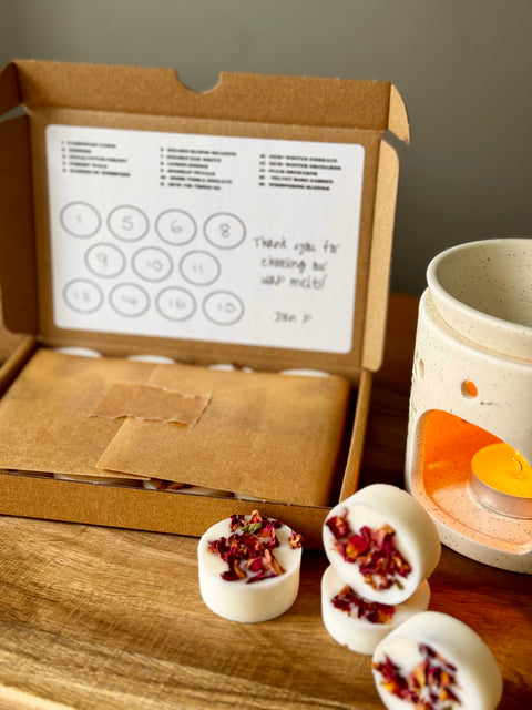 A kraft box of 11 natural botanical wax melts next to a wax warmer, styled with four loose melts on a wooden surface