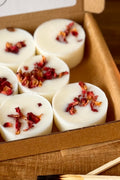 a close up shot of aroma quartz botanical wax melt pick and mix box, each melt is decorated with rose petals, on a wooden surface with match sticks
