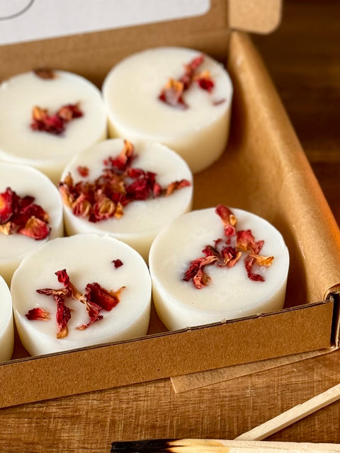 a close up shot of aroma quartz botanical wax melt pick and mix box, each melt is decorated with rose petals, on a wooden surface with match sticks
