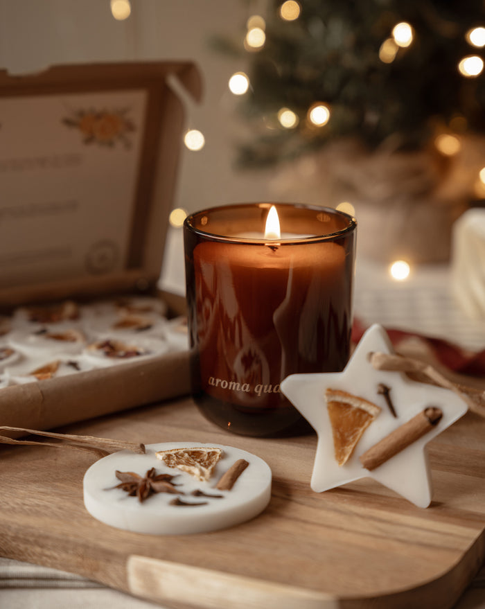 Winter Gathering Gift Box contents: a lit amber candle, star and circle scented wax decorations and a box of winter wax melts