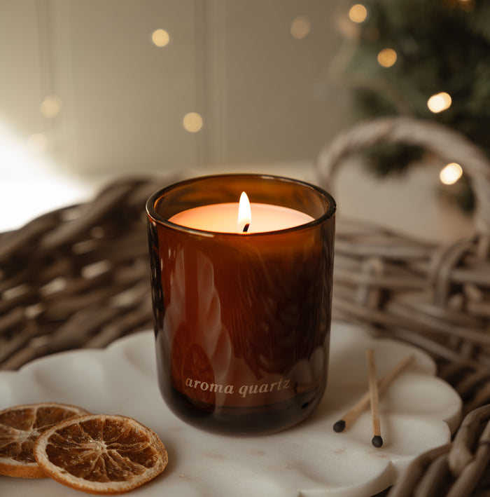 Aroma Quartz winter refillable coconut wax candle lit in an amber glass jar with dried orange slices