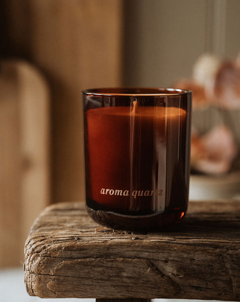 Brown candle in a glass holder labeled 'aroma quartz' on a wooden surface.