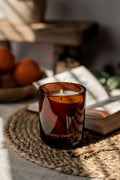 Brown glass candle with 'Aroma Quartz' on a woven mat with books and oranges in the background