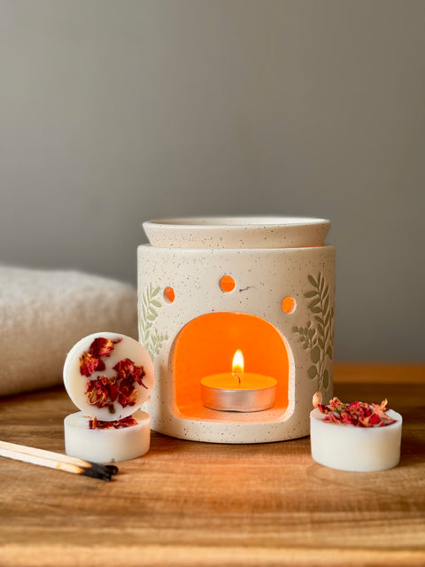 Aromatherapy oil burner with a candle inside on a wooden surface, surrounded by oil burner melts and match sticks.