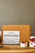 Box of Aroma Quartz Botanical Wax Melts on a wooden surface with a neutral background styled with oil burner melts and match sticks
