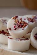 White round botanical wax melts with dried rose petals on a light surface