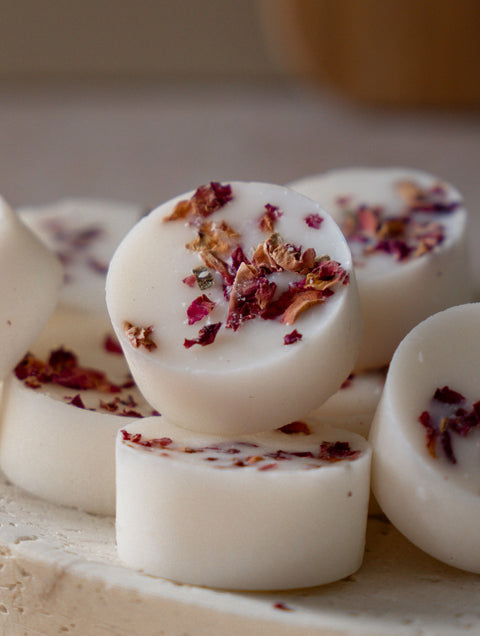 White round botanical wax melts with dried rose petals on a light surface