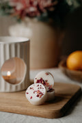 botanical wax melts with dried flowers on a wooden board with a candle and fruit in the background.