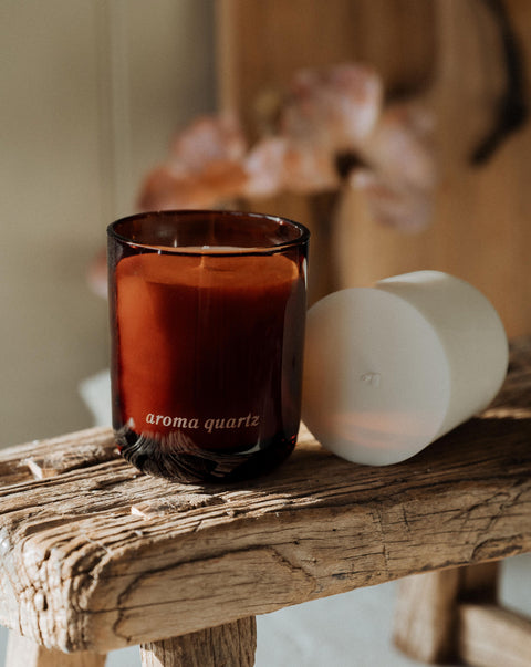 amber jar, refillable candle with candle refill next to it on a wooden stool and blurred background.
